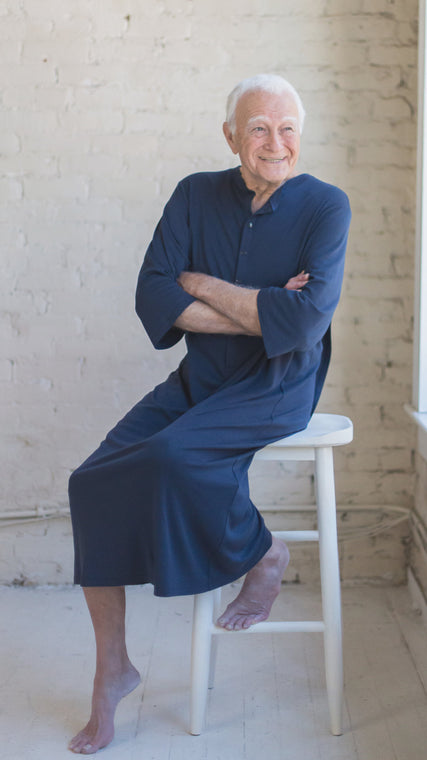 Load image into Gallery viewer, Man wearing mens hospital gown in cotton Henley in midnight blue, patient with arms crossed sitting on a stool
