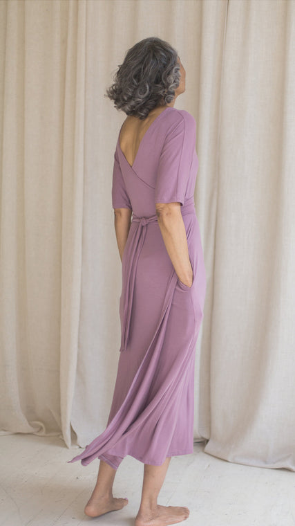 Load image into Gallery viewer, Woman wearing hospital patient gown, patient in lilac modal wrap dress, worn reversible, hand in pockets back view