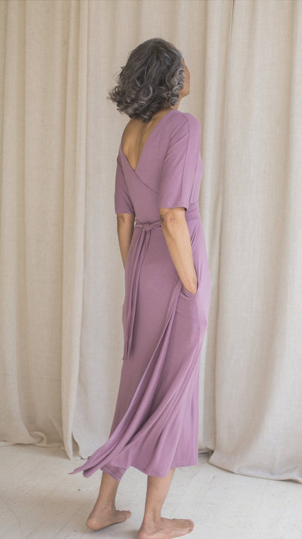 Load image into Gallery viewer, Woman wearing hospital patient gown, patient in lilac modal wrap dress, worn reversible, hand in pockets back view