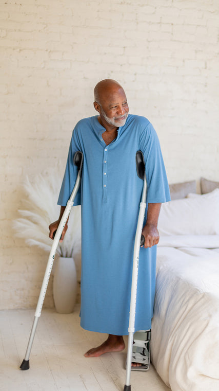 Load image into Gallery viewer, Modesty dressing in healthcare and clinical settings is known by Arkeras gown buyers as a key feature of use. Sleeves are near full length, yet flexible and open for IV access. Front non-metal snaps unbutton for medical staff easy access and the back has full coverage without restricting access for treatment or health care plans. Shown to be used with crutches, braces, gait belts, wheelchairs, and other supportive medical devices.