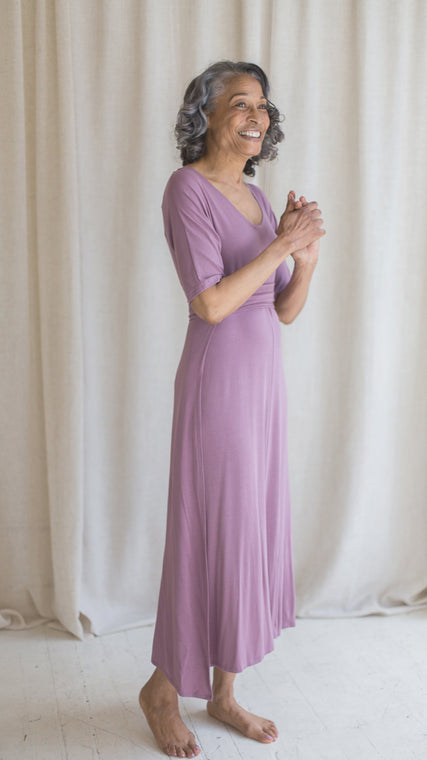 Woman wearing womens hospital gown, patient in lilac wrap dress style, standing with hands clasped
