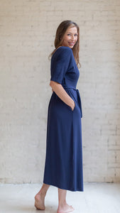 Woman wearing womens hospital gown, patient in navy blue wrap dress style with hands in pocket, side