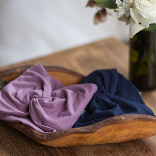 2 twist wrap headbands, lilac and blue, in a wooden bowl, best for keeping hair back or away from face during recovery or wearing a hospital gown