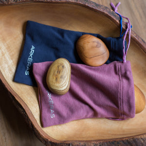 2 soothing brown stones on top of lilac and blue cotton pouches in a wooden bowl